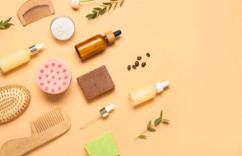 Hair scalp massager with shampoo bars, bottles of cosmetic products and brushes on beige background