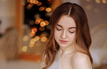 young beautiful woman in a knitted sweater and skirt sits on a bed against the backdrop of a christmax interior