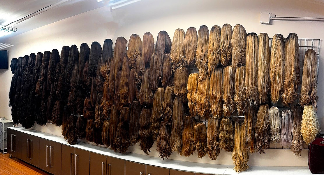 A wall display featuring numerous wigs in various shades of brown and blonde, arranged neatly on hooks above a row of cabinets.