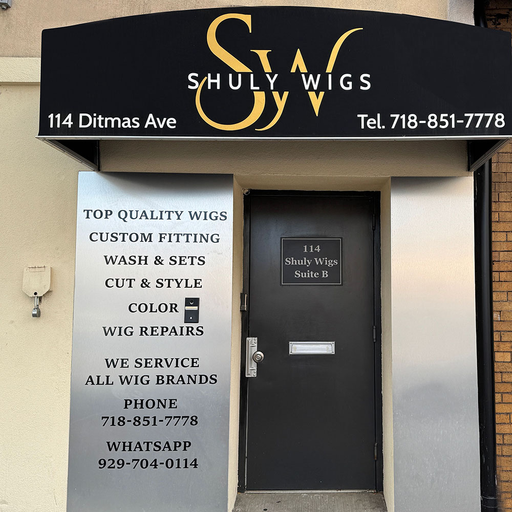 Storefront for Shuly Wigs with signage listing services such as custom fitting, washes, cuts, coloring, repairs, and contact information at 114 Ditmas Ave, Suite B.