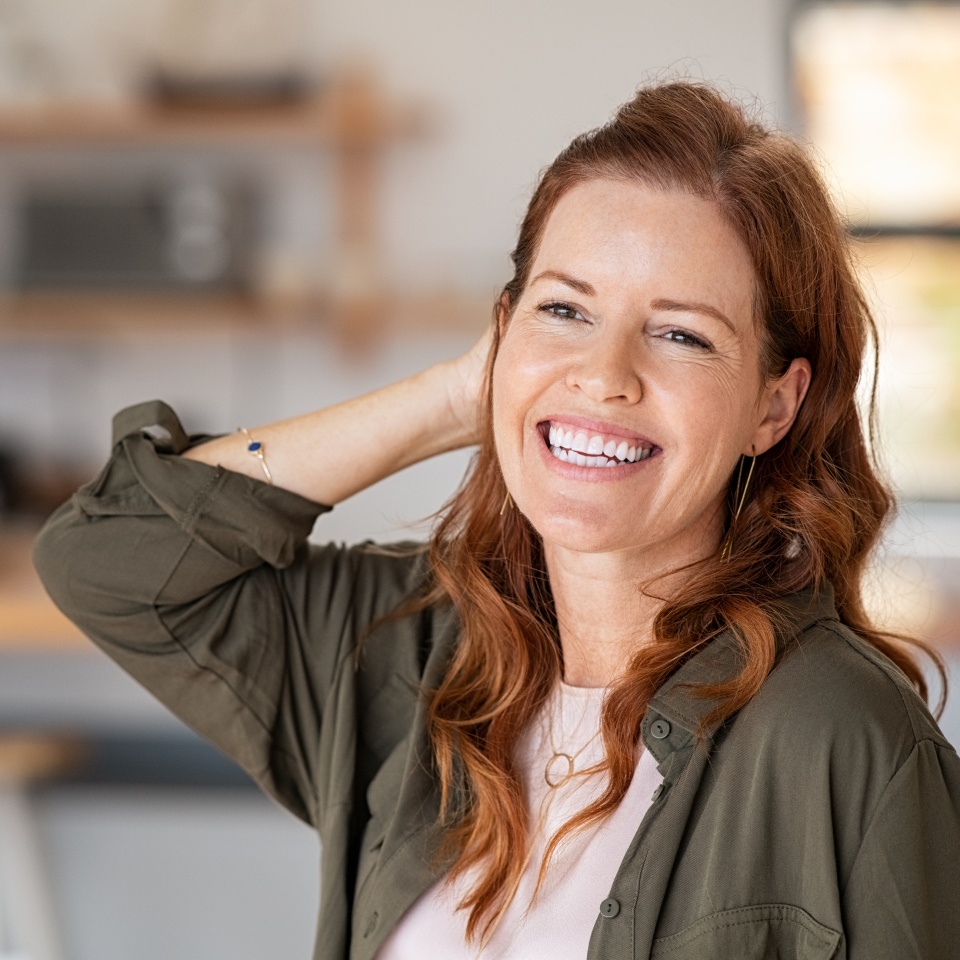 Portrait of beautiful mature woman at home. Successful middle aged woman smiling and looking away while touching hair. Mid redhead lady laughing and relaxing.