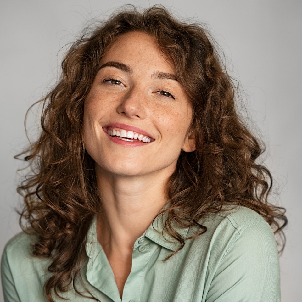 Close up face of beautiful young woman smiling and looking at camera isolated on grey background. Portrait of beauty natural girl with copy space. Female student in casual standing against gray wall.