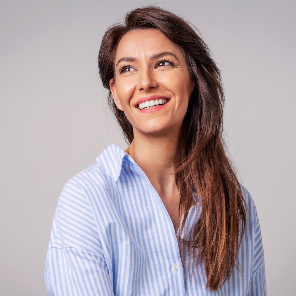 Smiling brunette businesswoman sitting against gray background. Confident female professional is wearing blue shirt. She is having brown hair. Copy space.