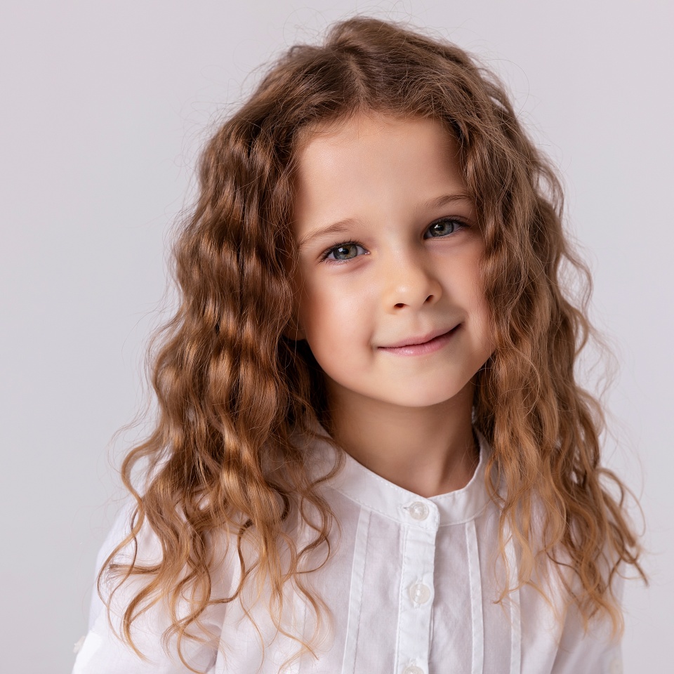 Laughing happy cheerful expression curly hair toddler girl in white shirt isolated on white background with copy space.
