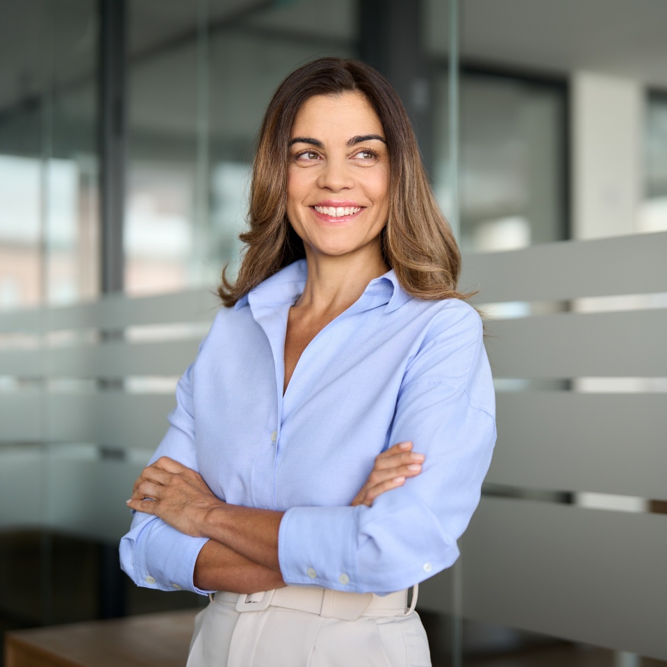 Happy confident mature professional business woman standing at work in office arms crossed looking away, proud hispanic middle aged businesswoman leader executive thinking of future success.
