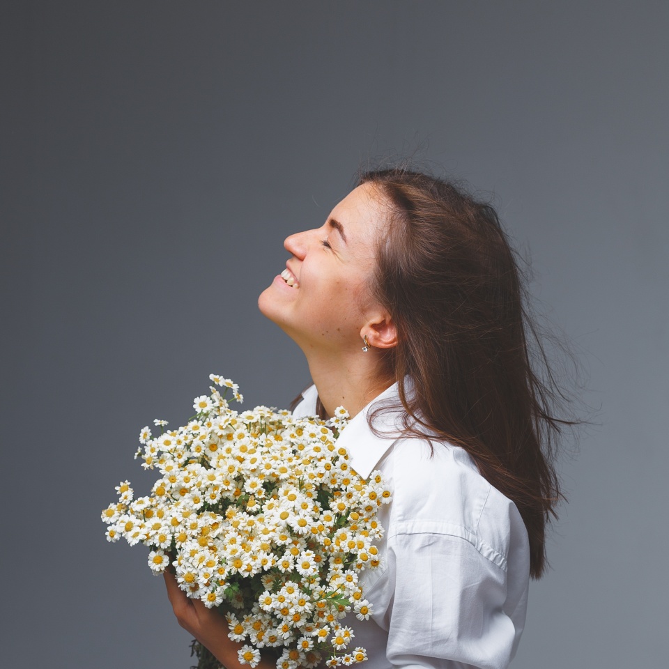 Studio portrait of young beautiful happy woman in white blouse with bouquet of daisies in hands