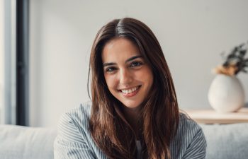 A young woman with long brown hair sits indoors