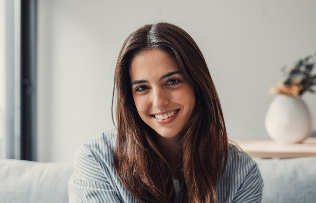 A young woman with long brown hair sits indoors