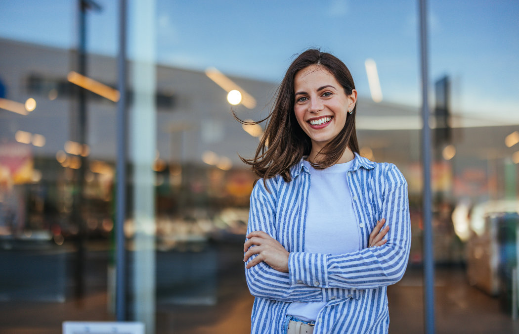 A woman with long brown hair smiles with arms crossed
