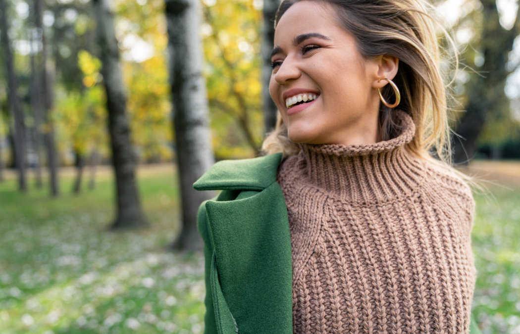 A person wearing a brown knit sweater and green coat stands outdoors
